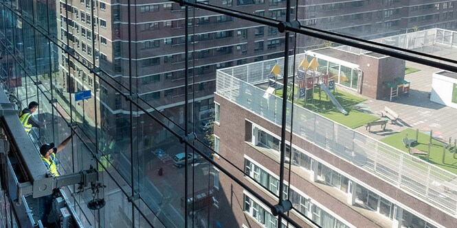 Arbeiter auf einem Gerüst beim Anbringen von Fensterfolien an einer Glasfassade
