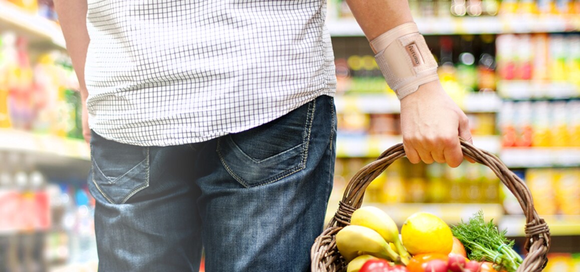 Mann mit Handgelenk-Bandage, der einen Korb mit Früchten trägt