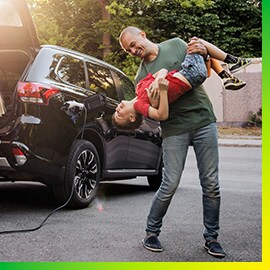Mann spielt mit Sohn neben einem schwarzen Auto, das in der Einfahrt geladen wird