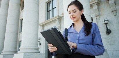 Frau an einem Tablet vor einem Verwaltungsgebäude
