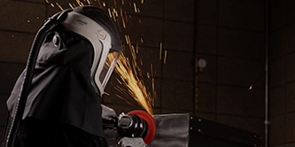 Arbeiter mit Schutzmaske schleift mit Scotch-Brite™ HD-Vliesscheibe eine Metalloberfläche
