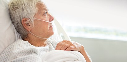 Een oudere vrouwelijke patiënt die uit het raam kijkt vanuit een ziekenhuisbed.
