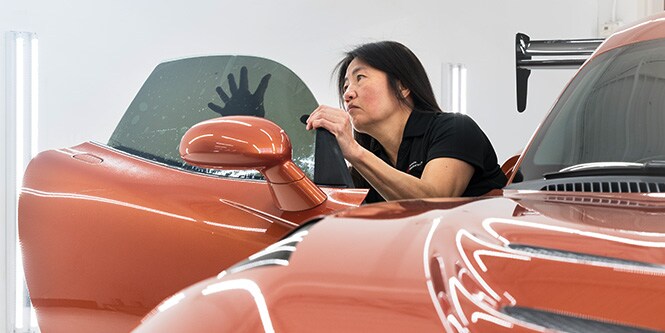 Eine Frau verklebt eine Scheibentönung innen auf der Beifahrerseite eines Sportwagens

