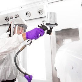 Ein Lackierer sprüht Füller auf ein Autoteil mit einem 3M Hochleistungslackierpistolensystem