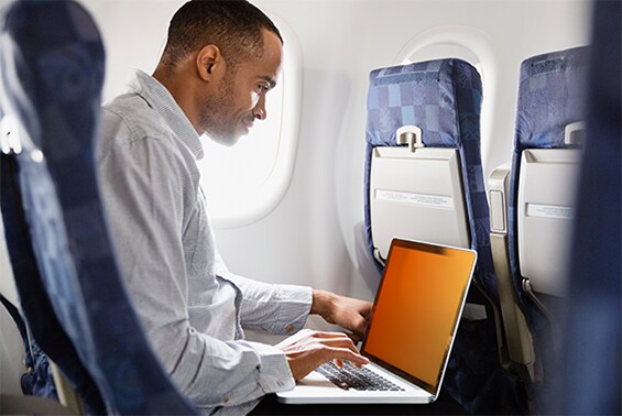 Mann, der in einem Flugzeug an einem Laptop mit dem Blickschutzfilter Gold arbeitet