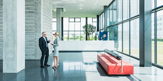 Lobby eines modernen Bürogebäudes mit zwei Geschäftsleuten, die sich unterhalten
