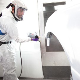 Ein Lackierer sprüht ein weißes Autoteil mit einem 3M Lackierpistolensystem