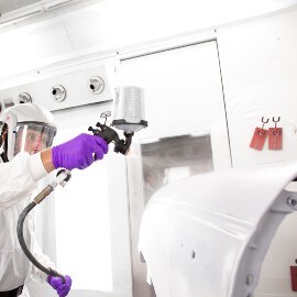 Ein Lackierer sprüht Füller auf ein Autoteil mit einem 3M Lackierpistolensystem