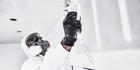 Professioneller Dekorateur streicht eine Decke und trägt dabei vollständige PSA von 3M

